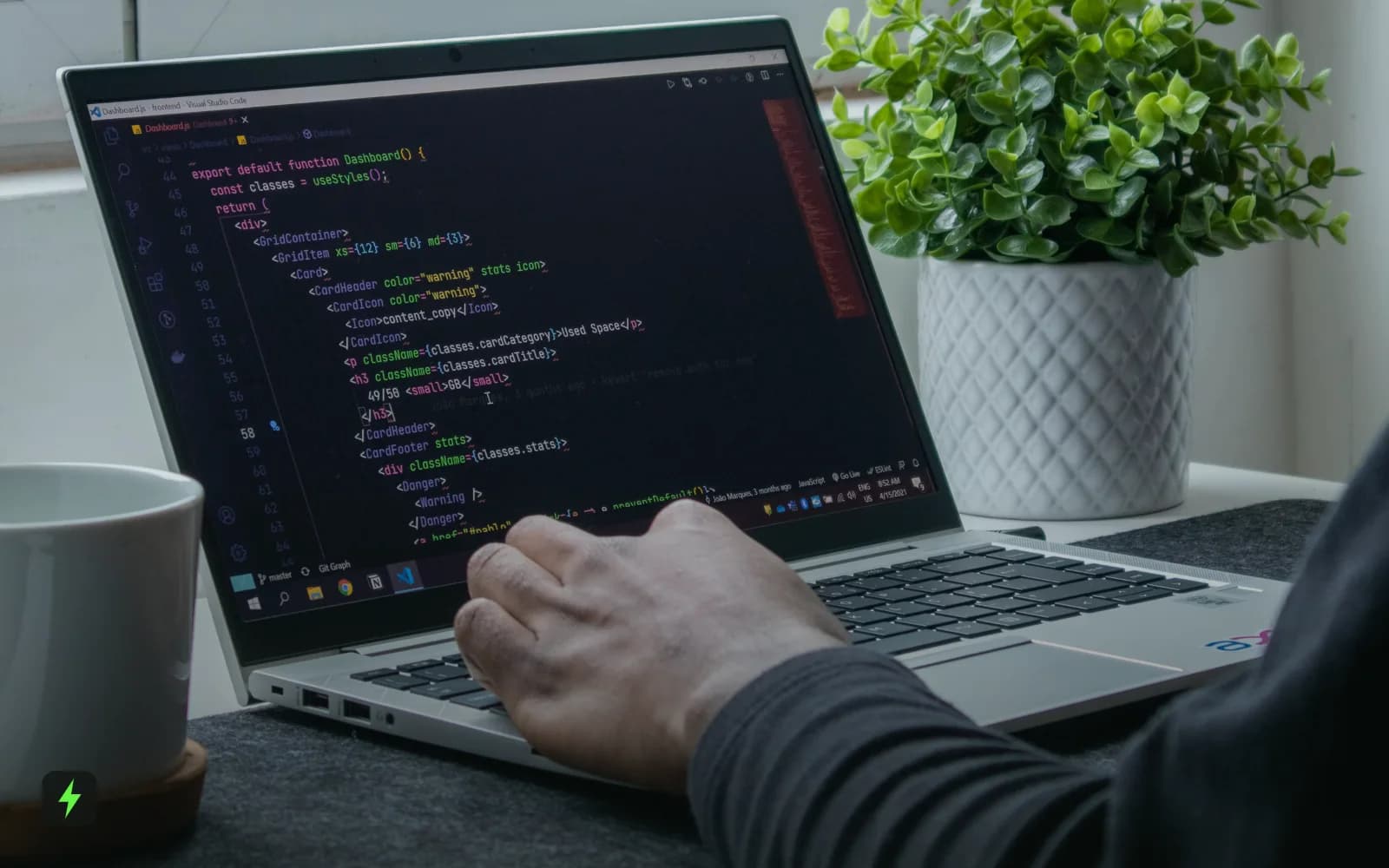 A developer writing code on a laptop beside a plant